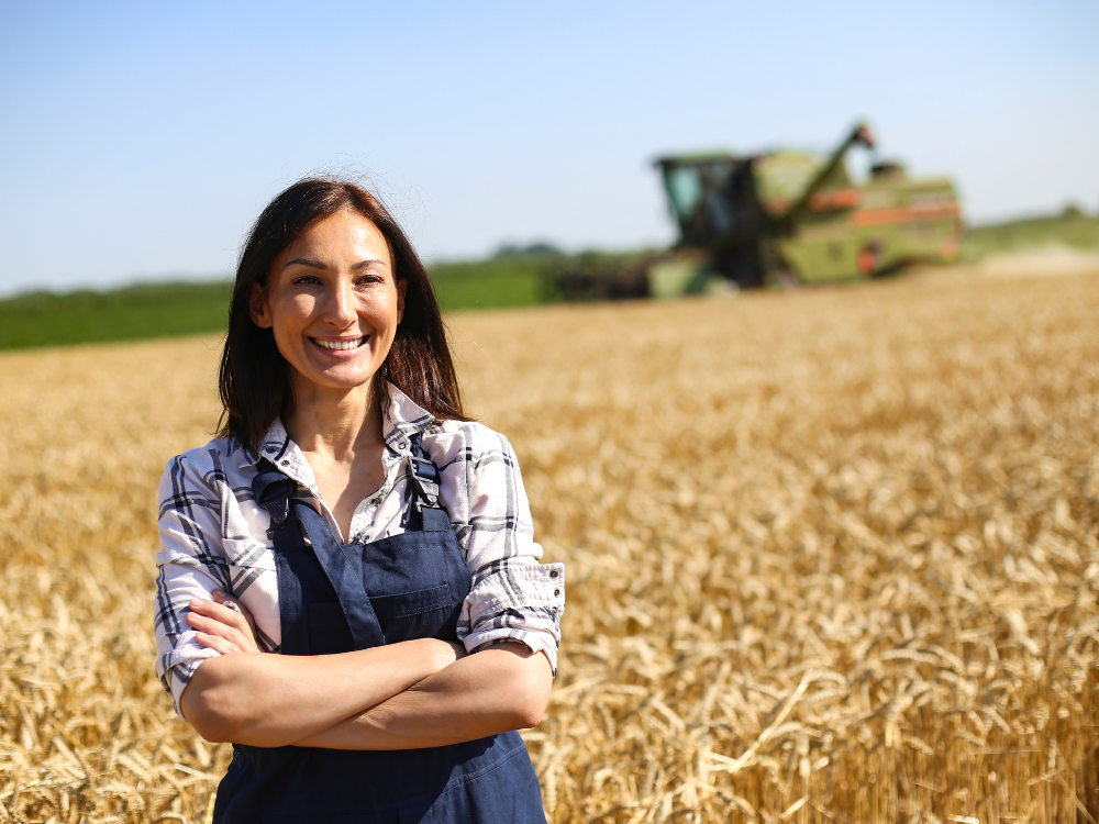 Farm owner standing in field smiling with arms crossed and combine tractor in background