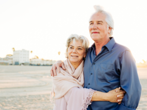 Older man and woman couple standing on a beach smiling looking off into the distance