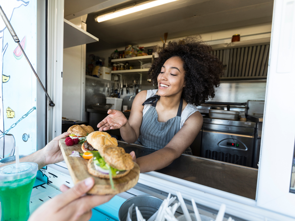Young woman inside of a food truck handing over a platter of food she just made to a customer