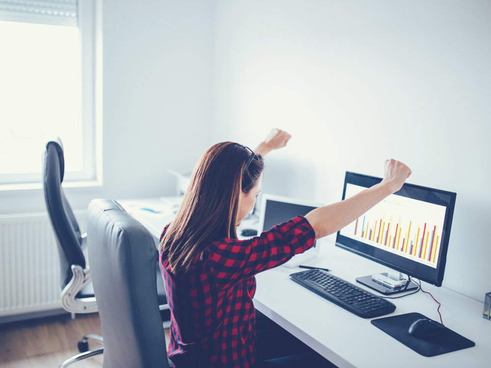 Woman sitting at a computer with her fists in the air celebrating