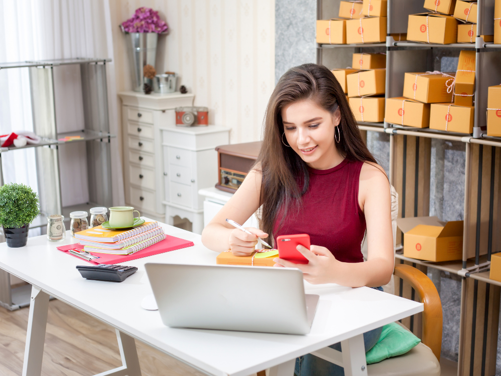 online business owner sitting with pen and phone in hand with boxes in the background