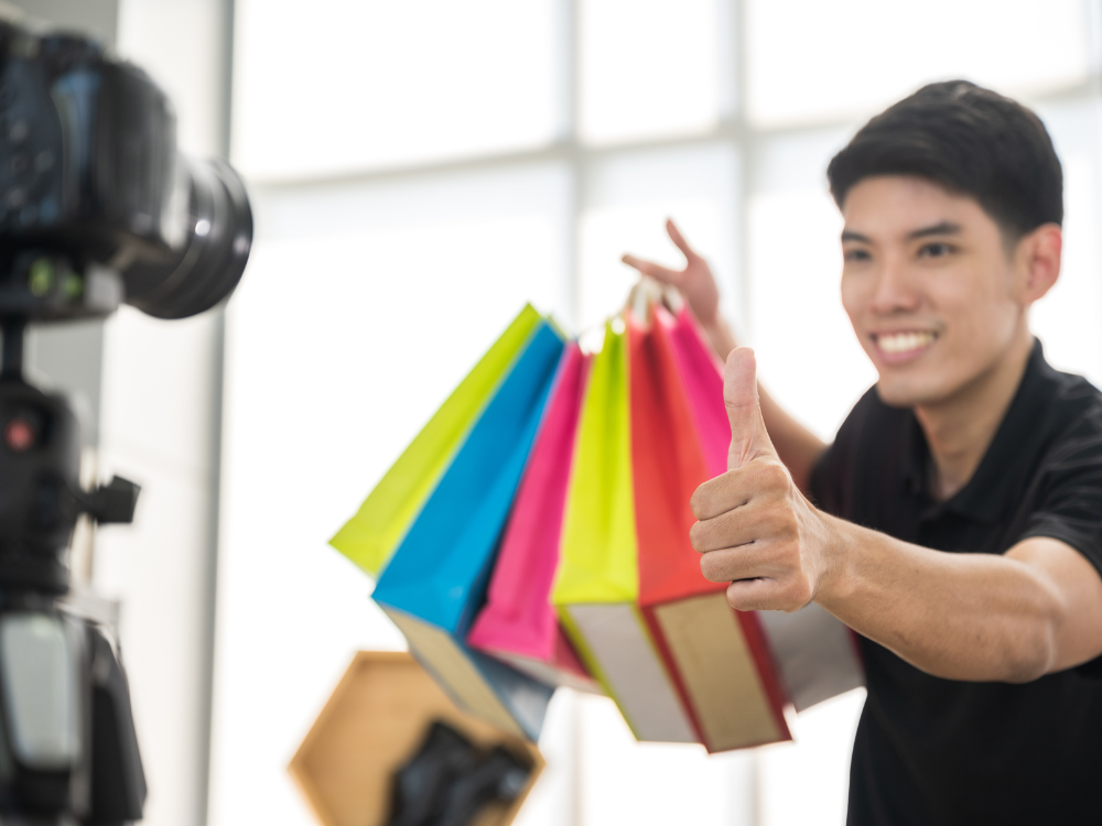 young man holding colorful shopping bags in front of camera filming a commercial