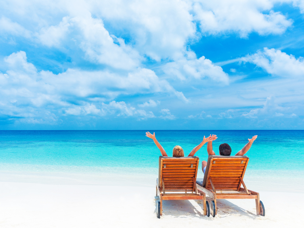 Two people sitting on beach chairs with arms in the air on the beach happy