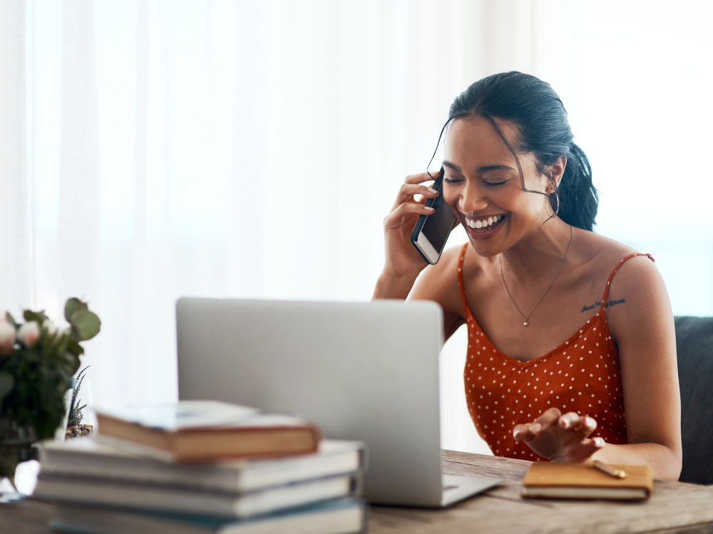 woman sitting in front of computer talking on phone and smiling