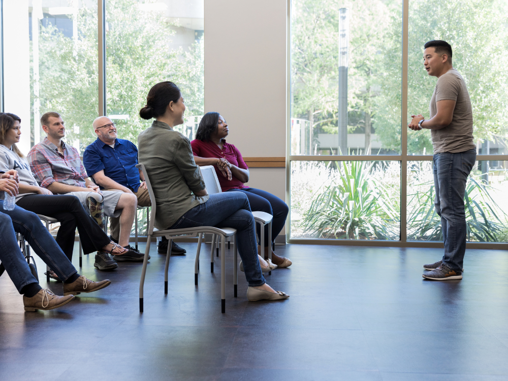 Man standing in front of room presenting to happy people sitting in chairs