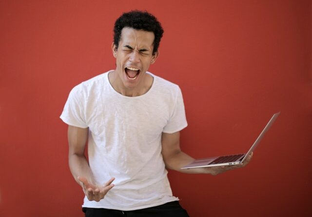 young man yelling in frustration while holding a computer