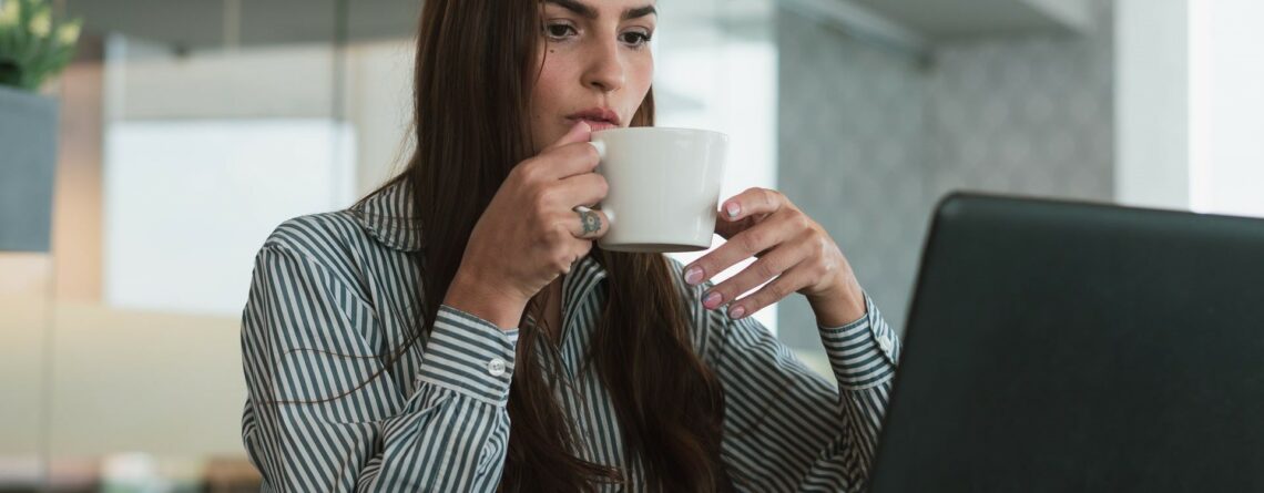 business woman drinking a coffee while looking at her computer screen