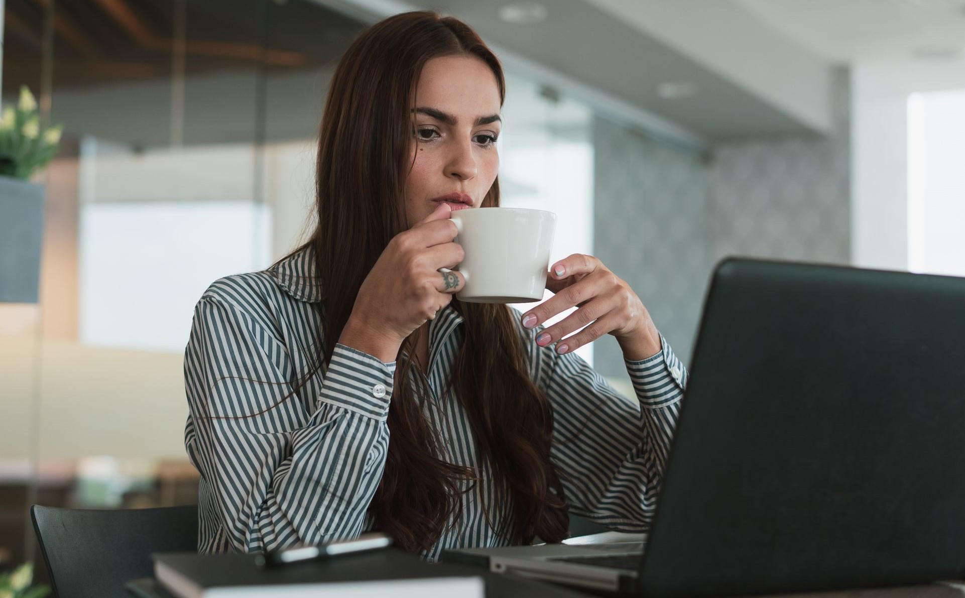 business woman drinking a coffee while looking at her computer screen